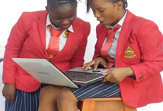 Two students in red blazers working together on a laptop
